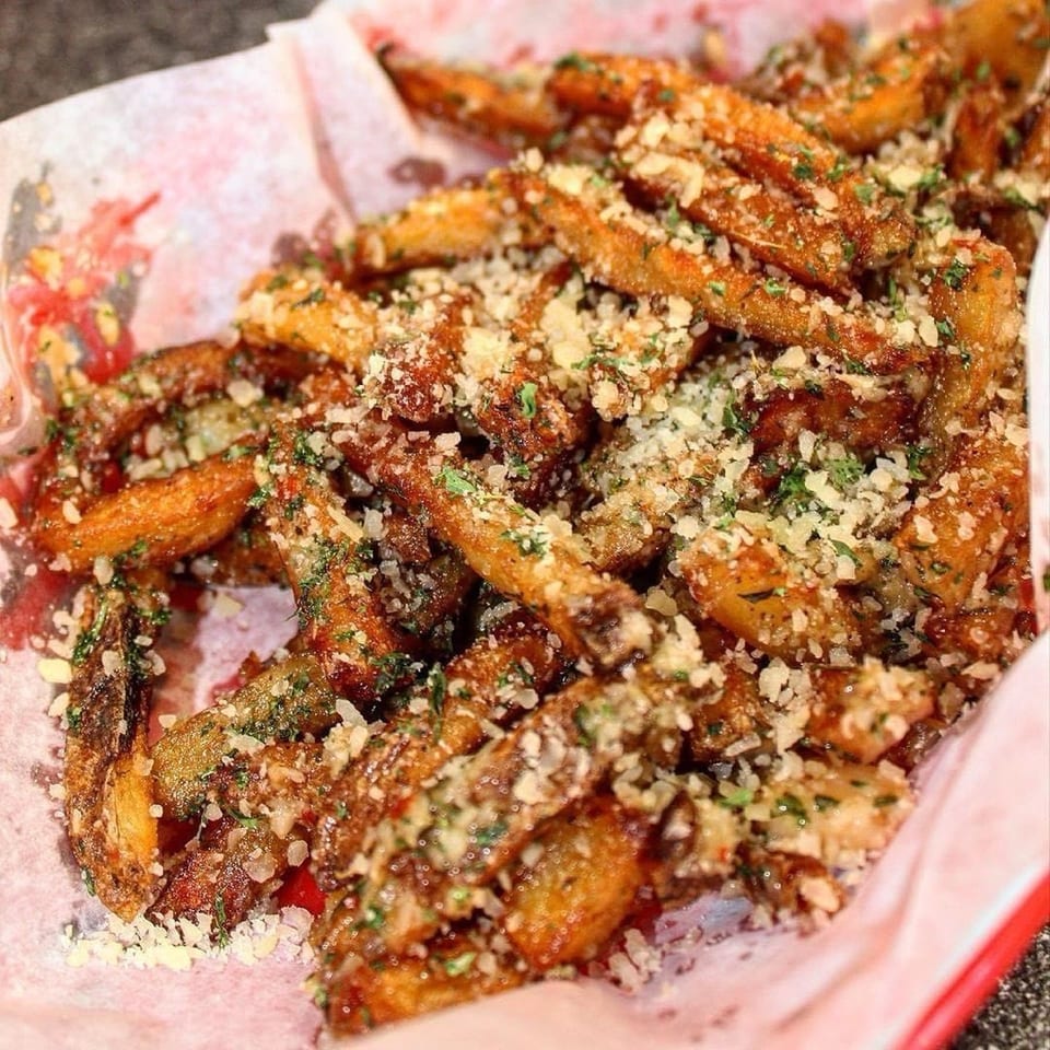 Crispy Wiz Kidz Cheesesteaks fries topped with grated cheese and green herbs in a red basket.