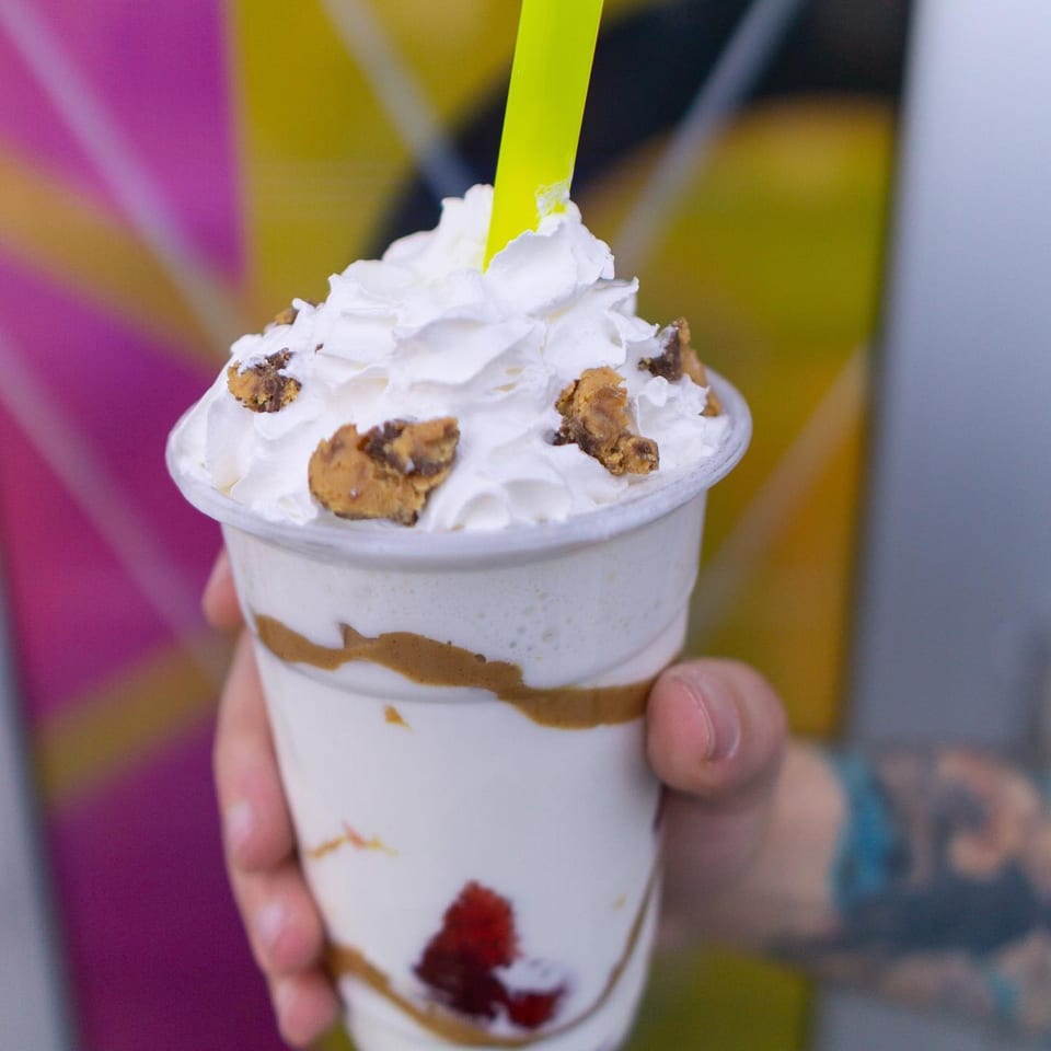 Hand holding a Wiz Kidz milkshake with whipped cream, cookie crumbles, and a neon straw.